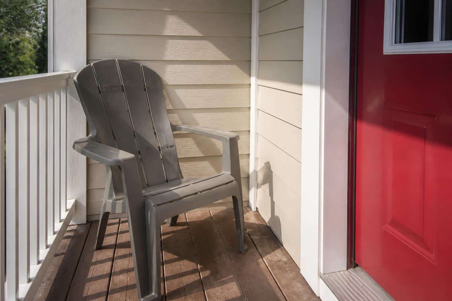 A gray plastic Adirondack chair beside a porch doorway showing tight clearance space on a small porch