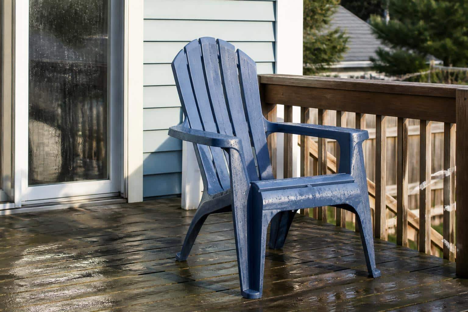 A freshly washed blue plastic Adirondack chair drying in sunlight, water droplets on the slats