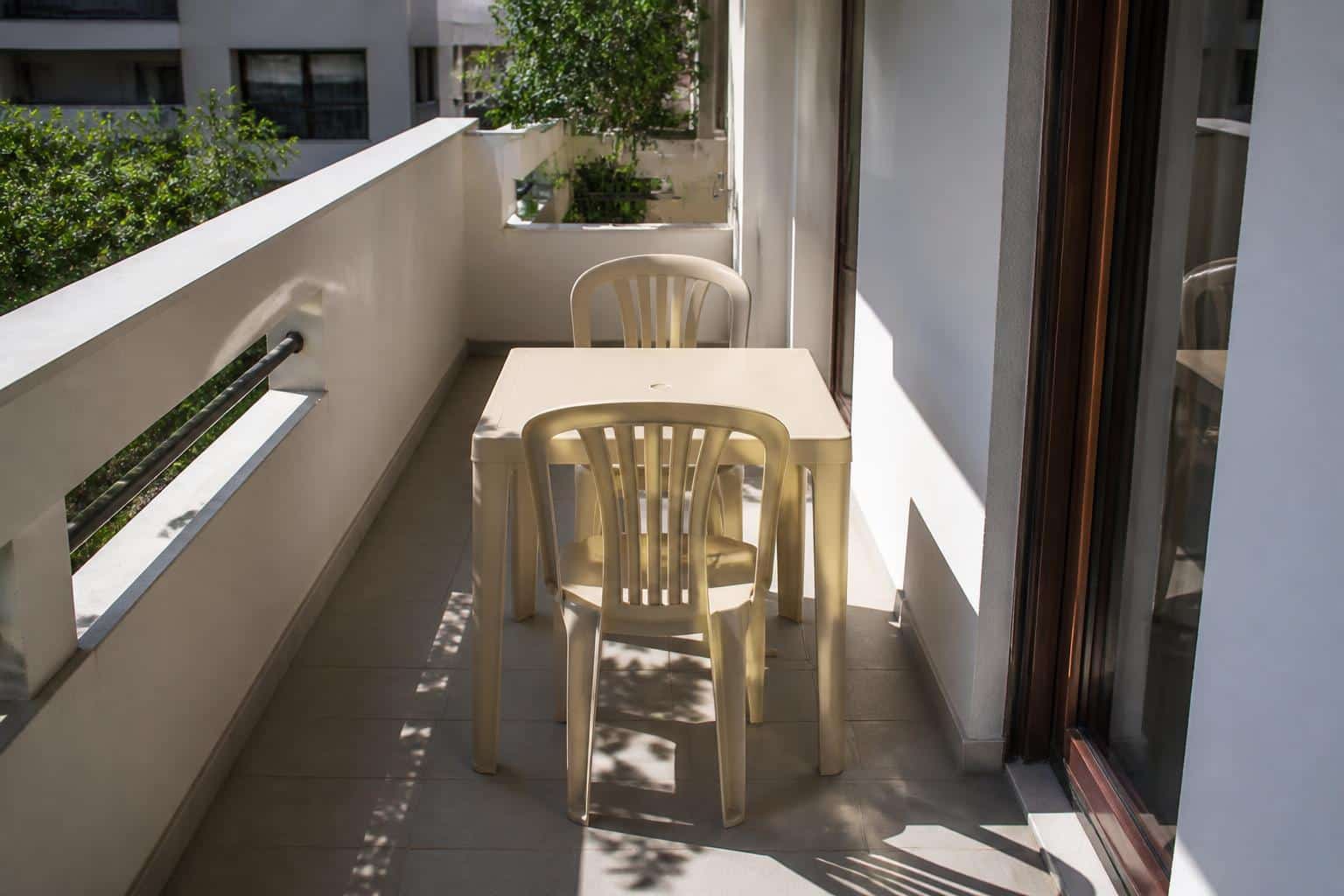 Two slim armless plastic dining chairs at a small dining-height plastic table on a narrow apartment balcony leaving walking room