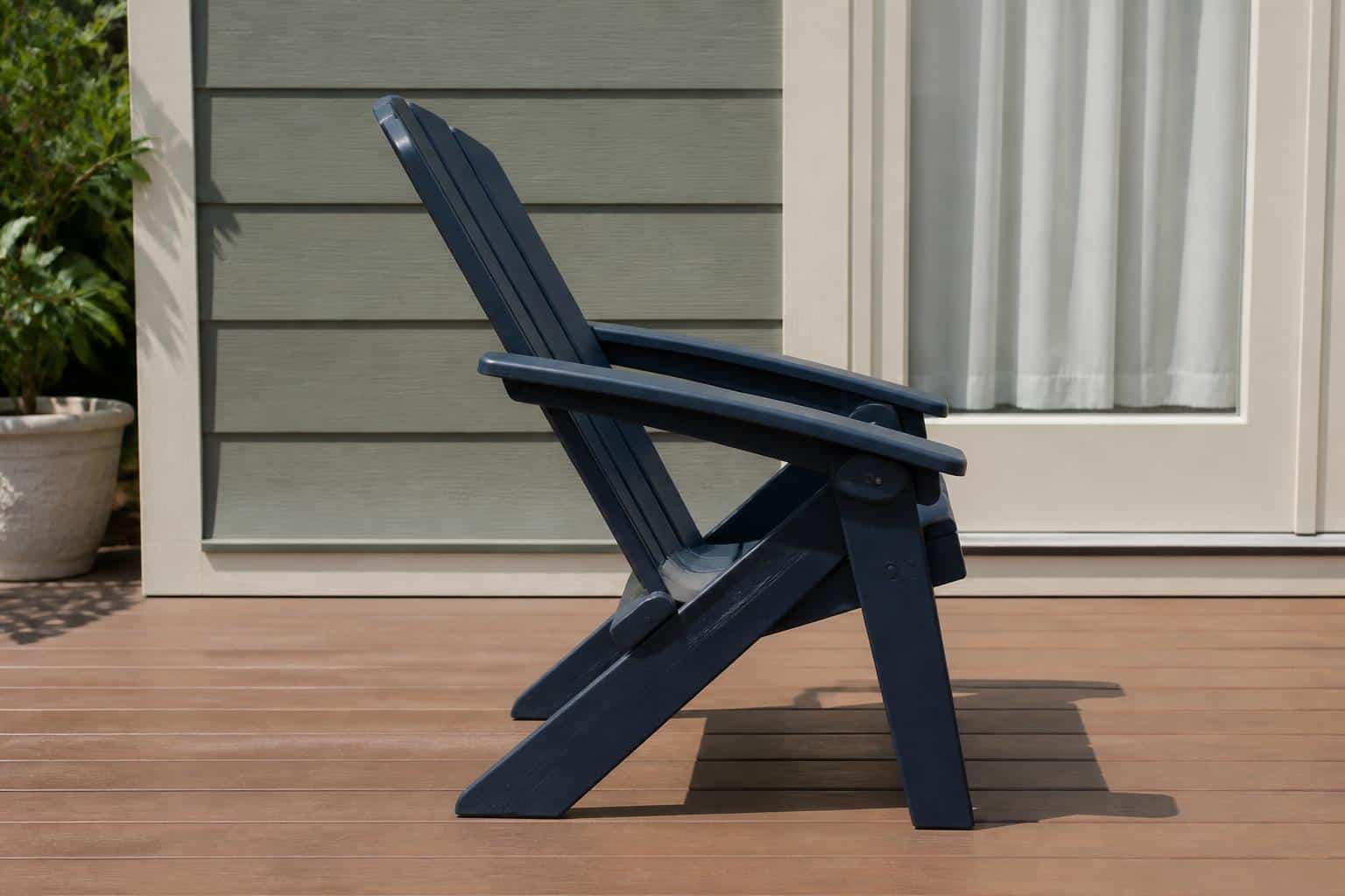 Side view of a navy folding plastic Adirondack chair on a deck with its folding hinge mechanism clearly visible, molded plastic construction