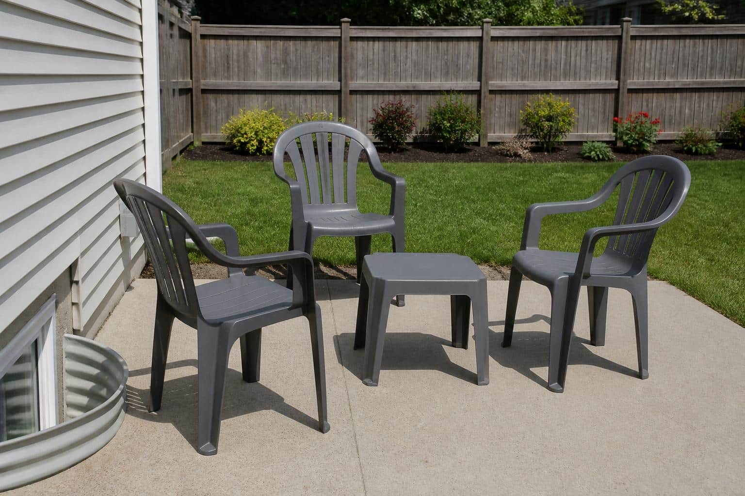 A matching set of glossy gray plastic patio chairs and a small plastic table on a backyard patio, uniform solid color