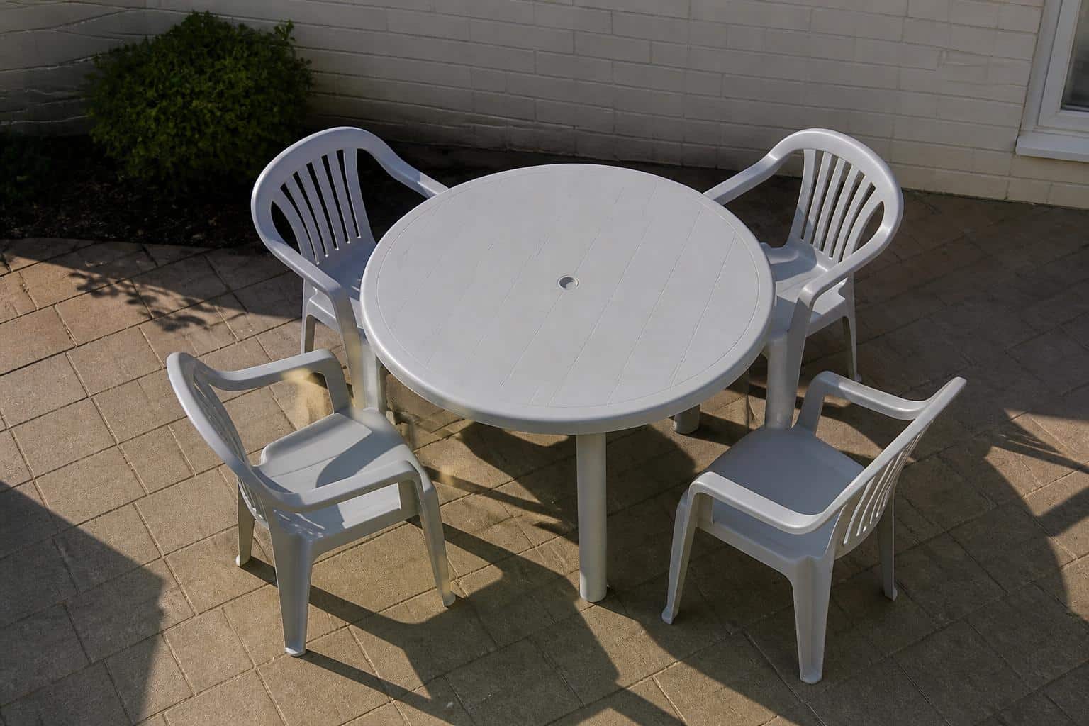 High-angle view of a round molded plastic patio table with a plank-style molded top and four glossy plastic dining chairs arranged around it showing seat spacing