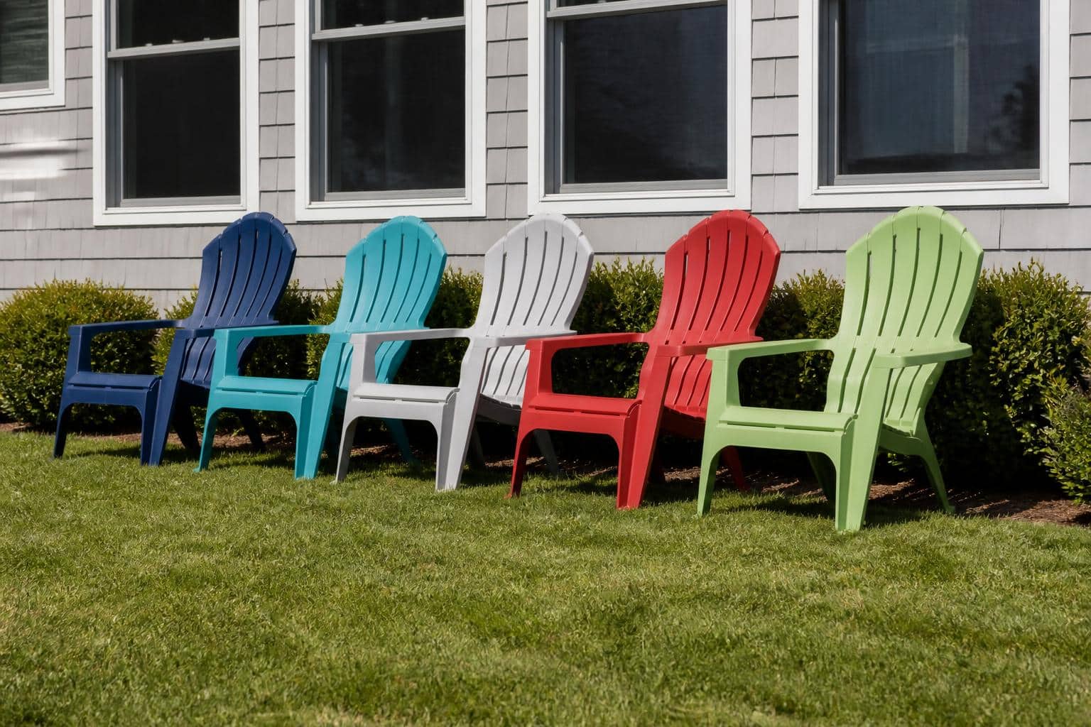 A row of plastic Adirondack chairs in assorted colors lined up on a lawn