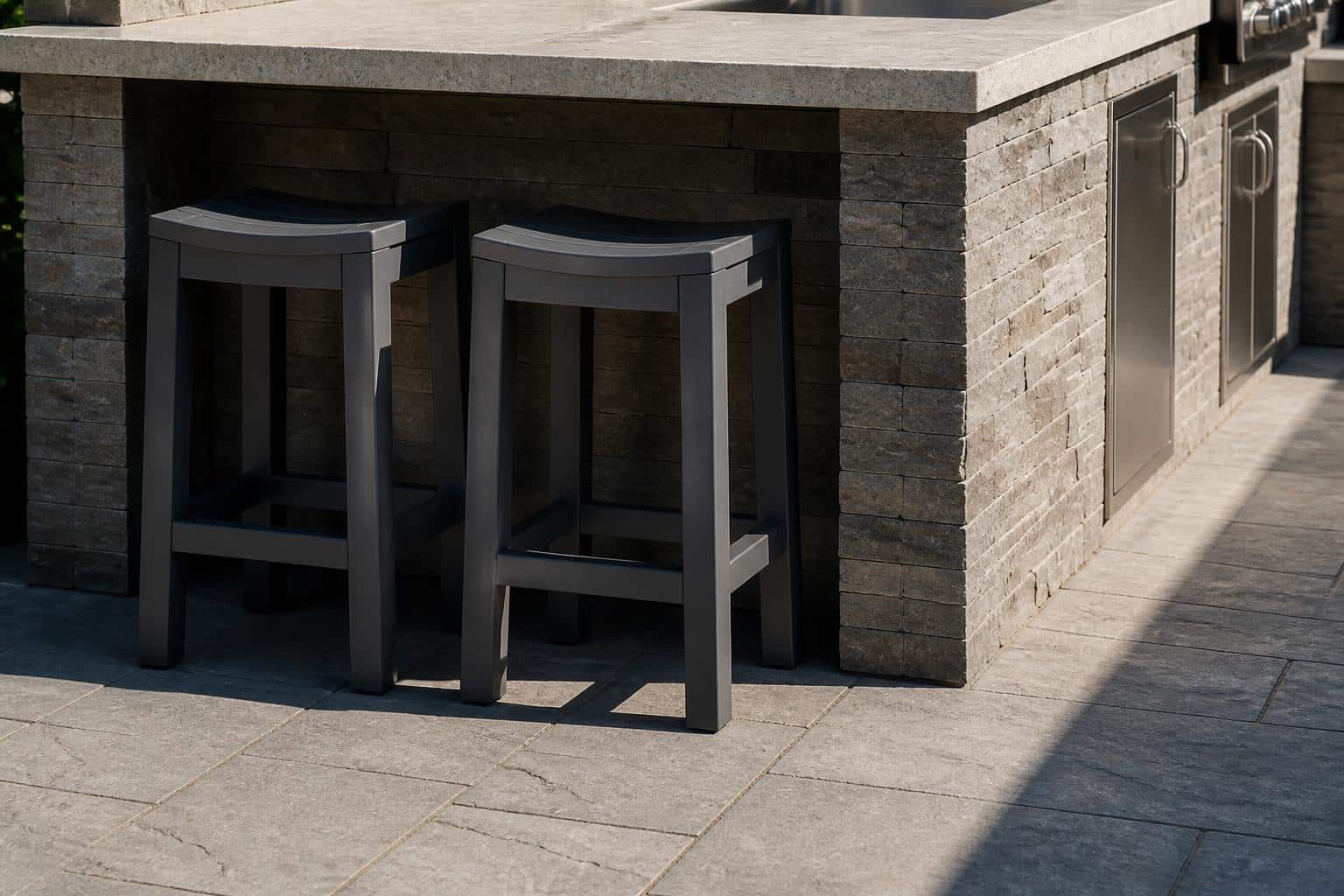Two charcoal gray plastic counter-height stools tucked under an outdoor kitchen island bar overhang