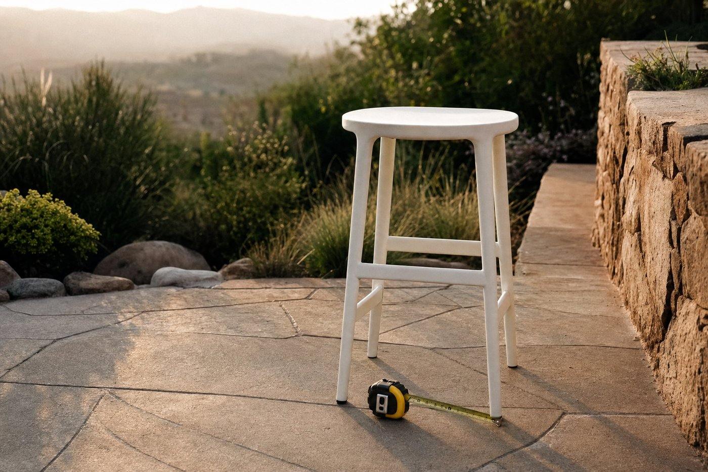 White outdoor stool beside a tape measure on a stone patio
