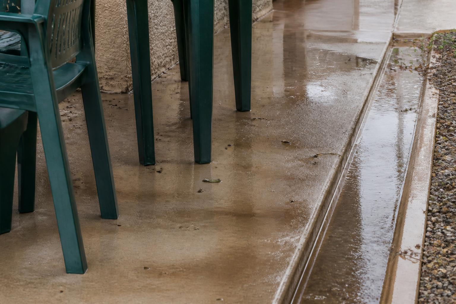 Outdoor chair and table legs beside a wet Tucson patio drainage path