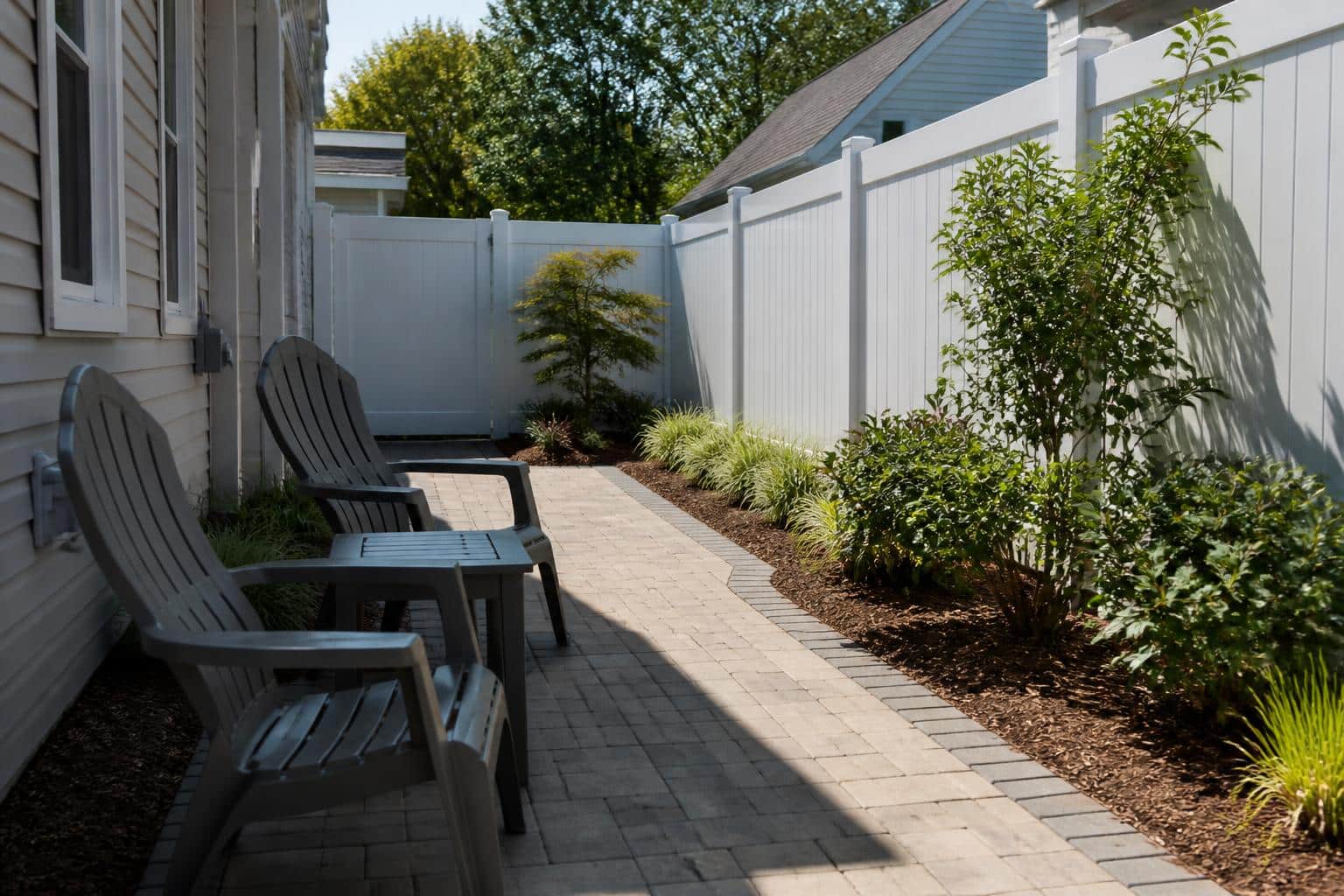 A small paver patio with two plastic chairs and a plastic end table placed against one edge leaving a clear walking path