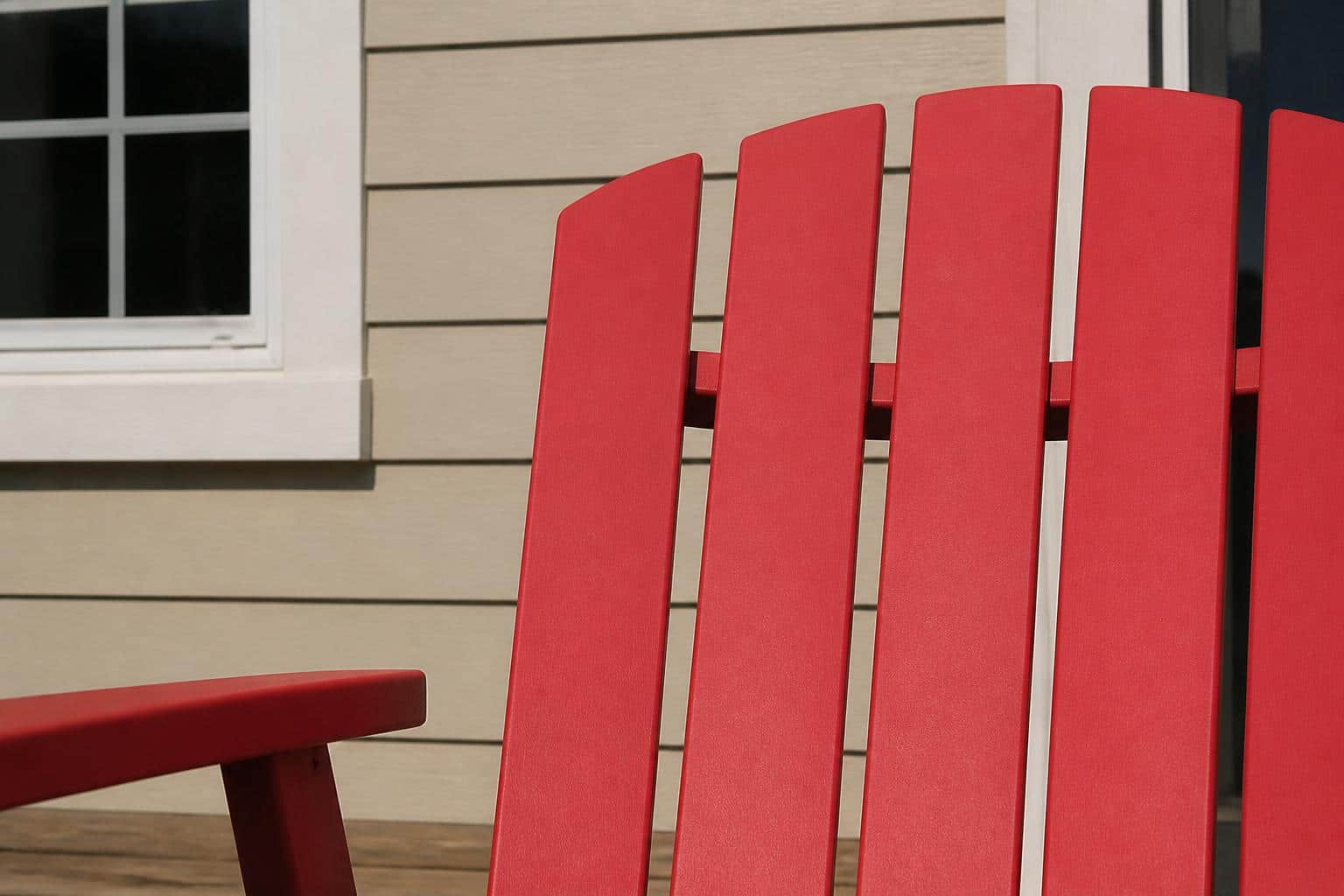 Close-up of bright red plastic Adirondack chair back slats in full direct sunlight, smooth solid surface