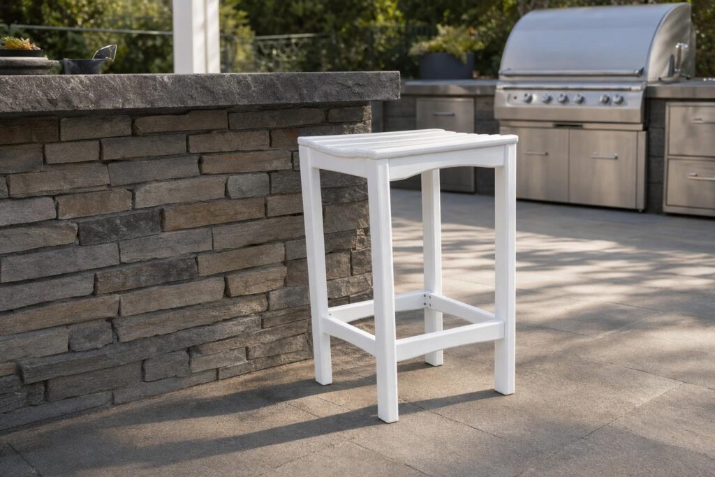 A white counter height stool beside a stone outdoor bar counter with a grill in the background