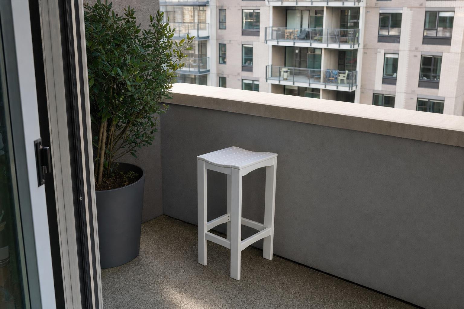 A white counter height stool in the corner of a city balcony