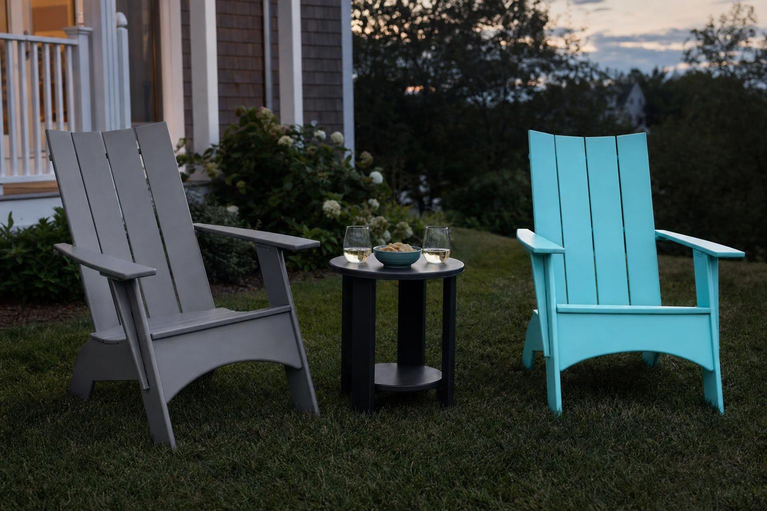 A round end table between two Adirondack chairs holding glasses and a bowl at dusk